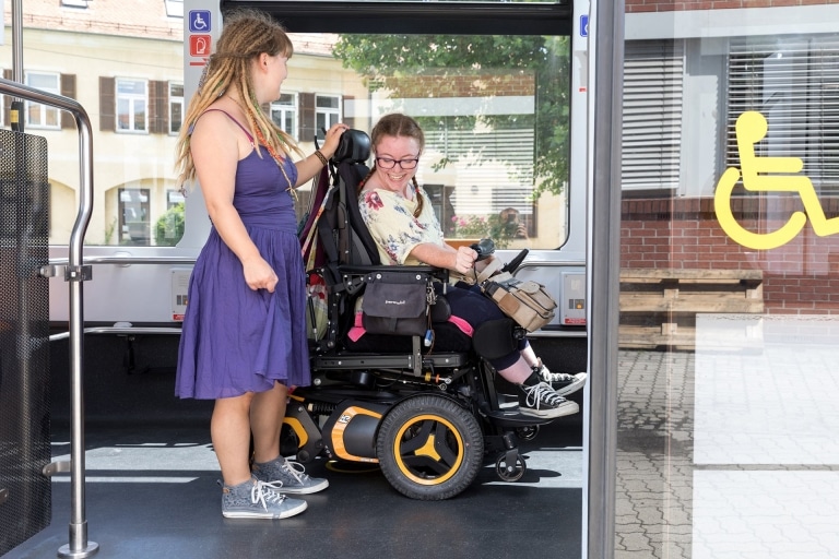 Zwei junge Frauen fahren selbstbestimmt Straßenbahn, eine davon sitzt im Rollstuhl