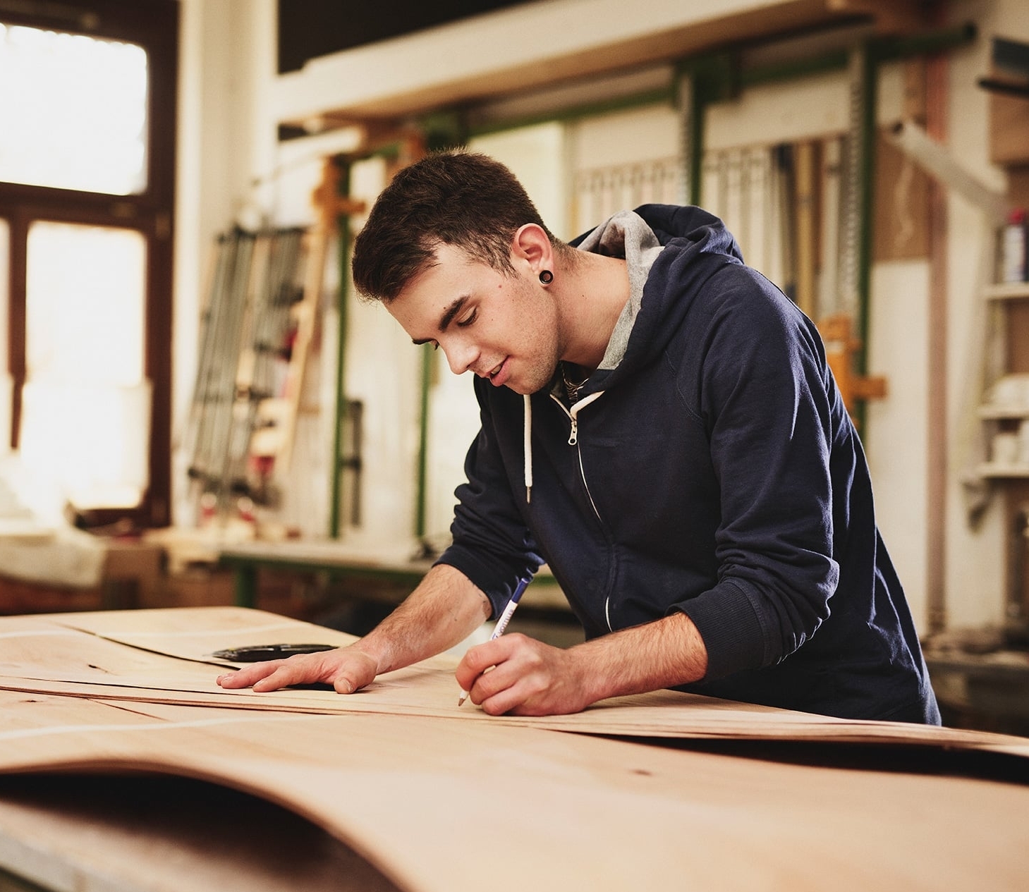 junger Mann zeichnet Holzplatte in erfa Tischlerei an