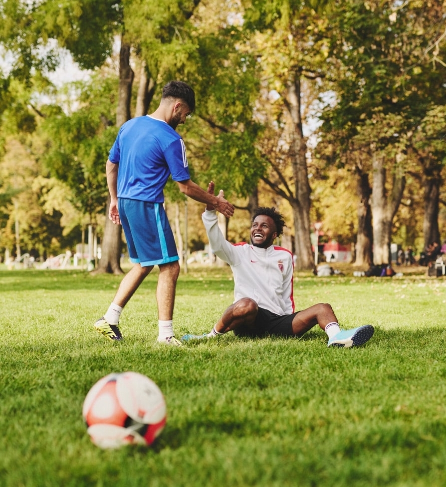 zwei junge Männer auf Fußballfeld, einer hilft dem anderen von Boden hoch