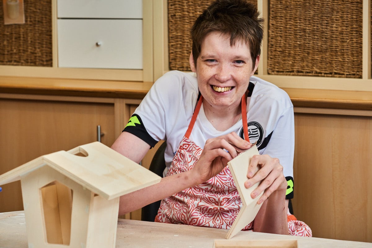junger Mann mit Behinderungen schleift Vogelhaus aus Holz in Holzatelier Karlschacht