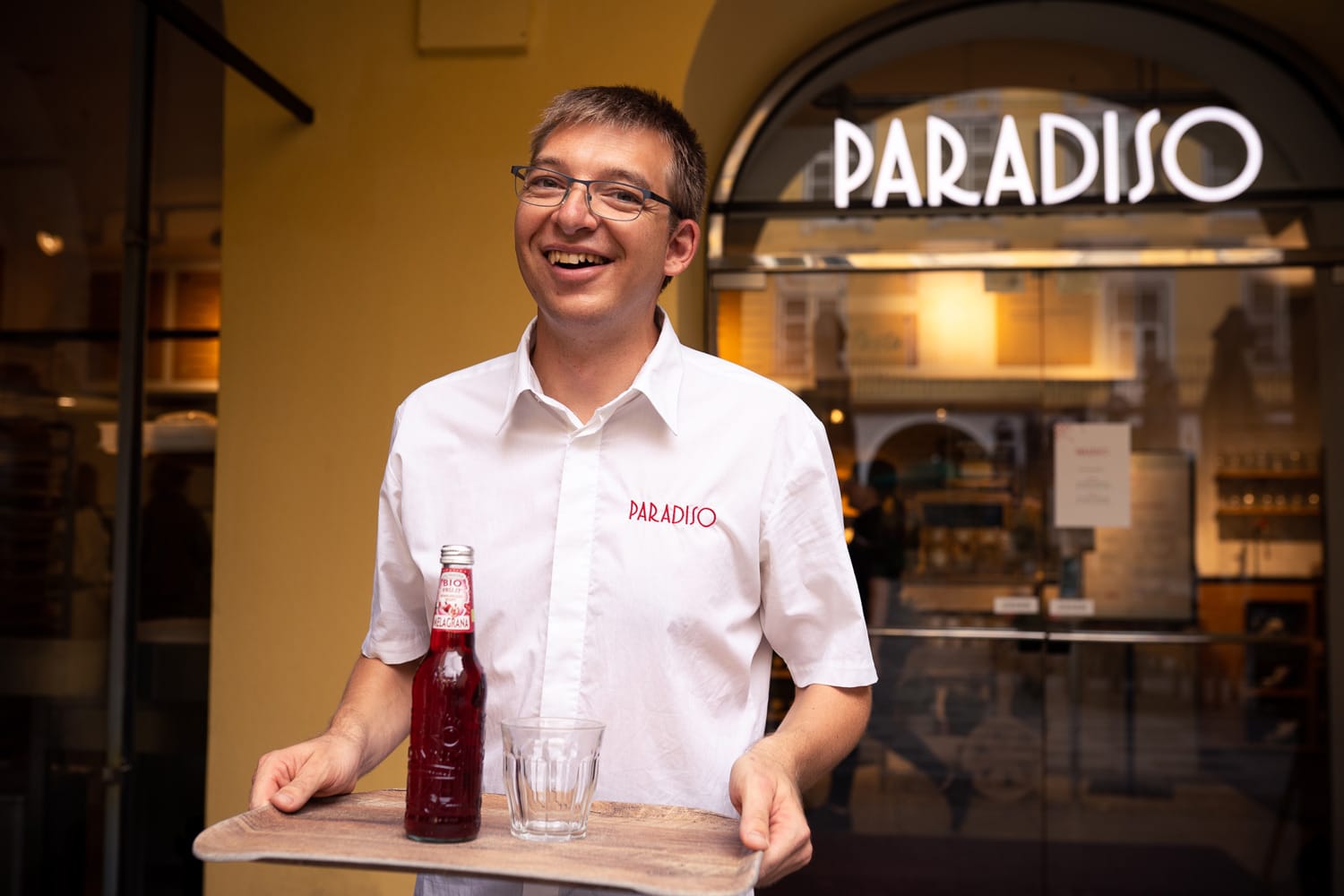 junger Kellner serviert Getränke, steht vor Lokal Paradiso