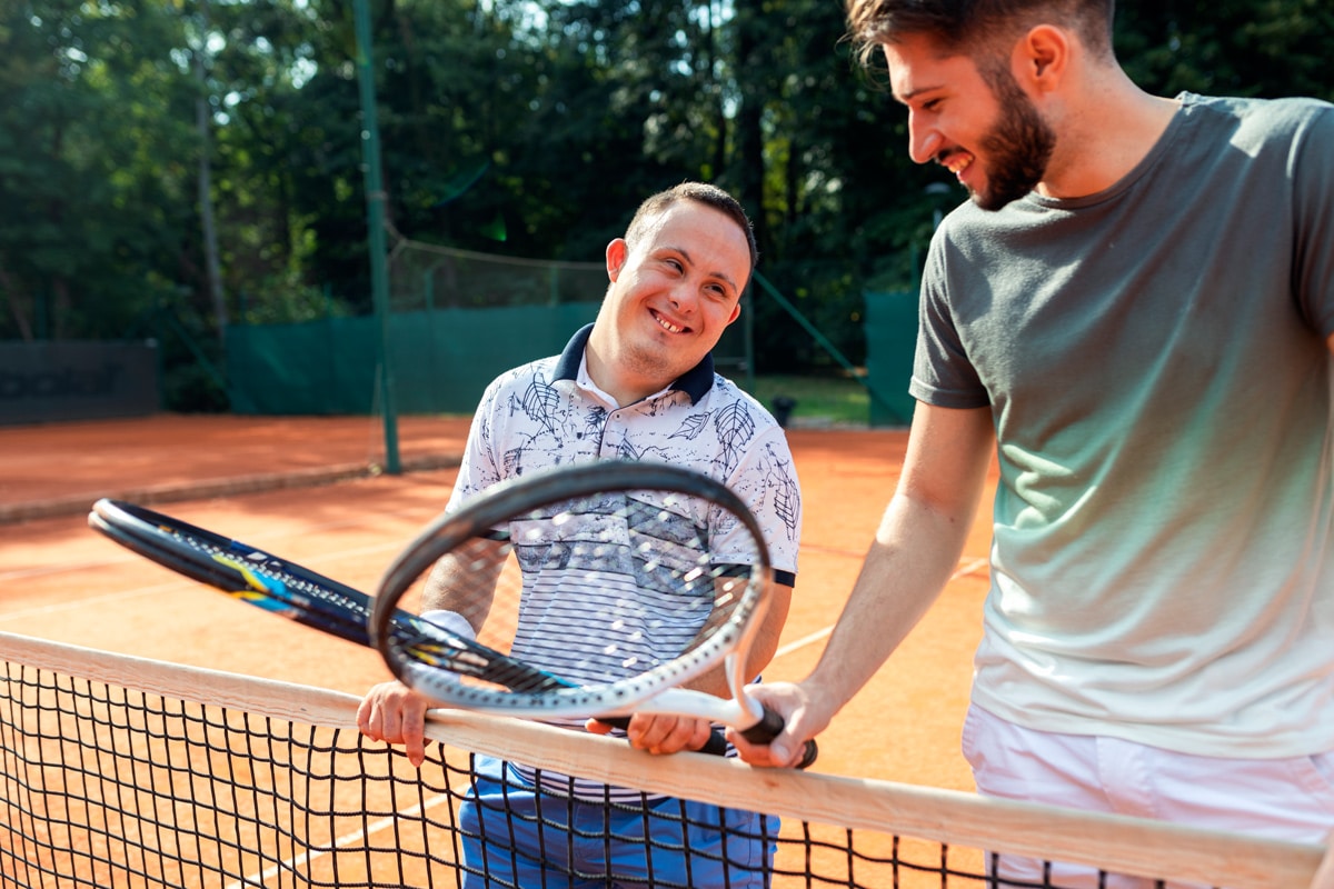 junger Mann mit Downsyndrom mit Tennislehrer stehen bei Tennisnetz