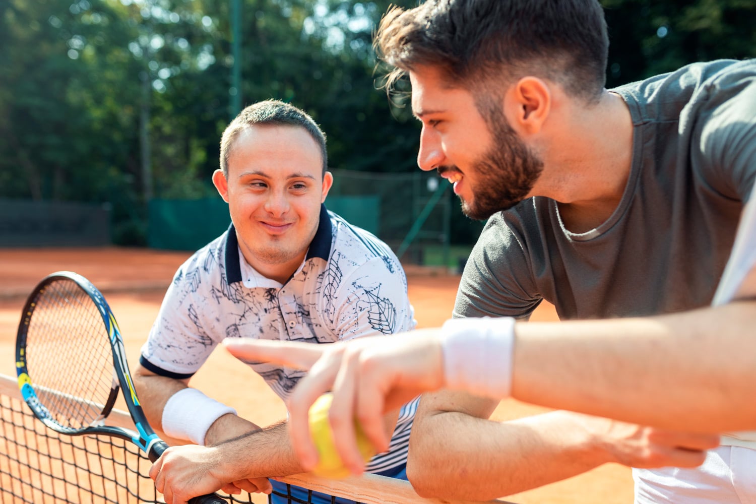junger Mann mit Downsyndrom mit Tennislehrer auf Tennisplatz