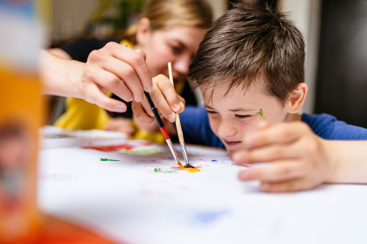 Autistischer Junge konzentriert beim Malen mit Betreuerin bei Sommerbetreuung