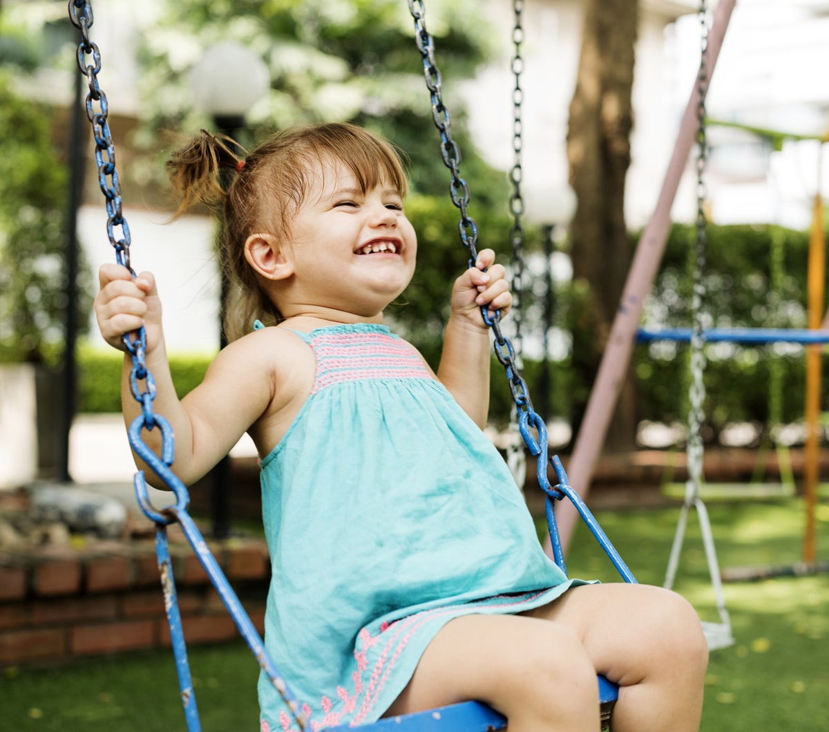 kleines Mädchen schaukelt lachend während der Sommerbetreuung