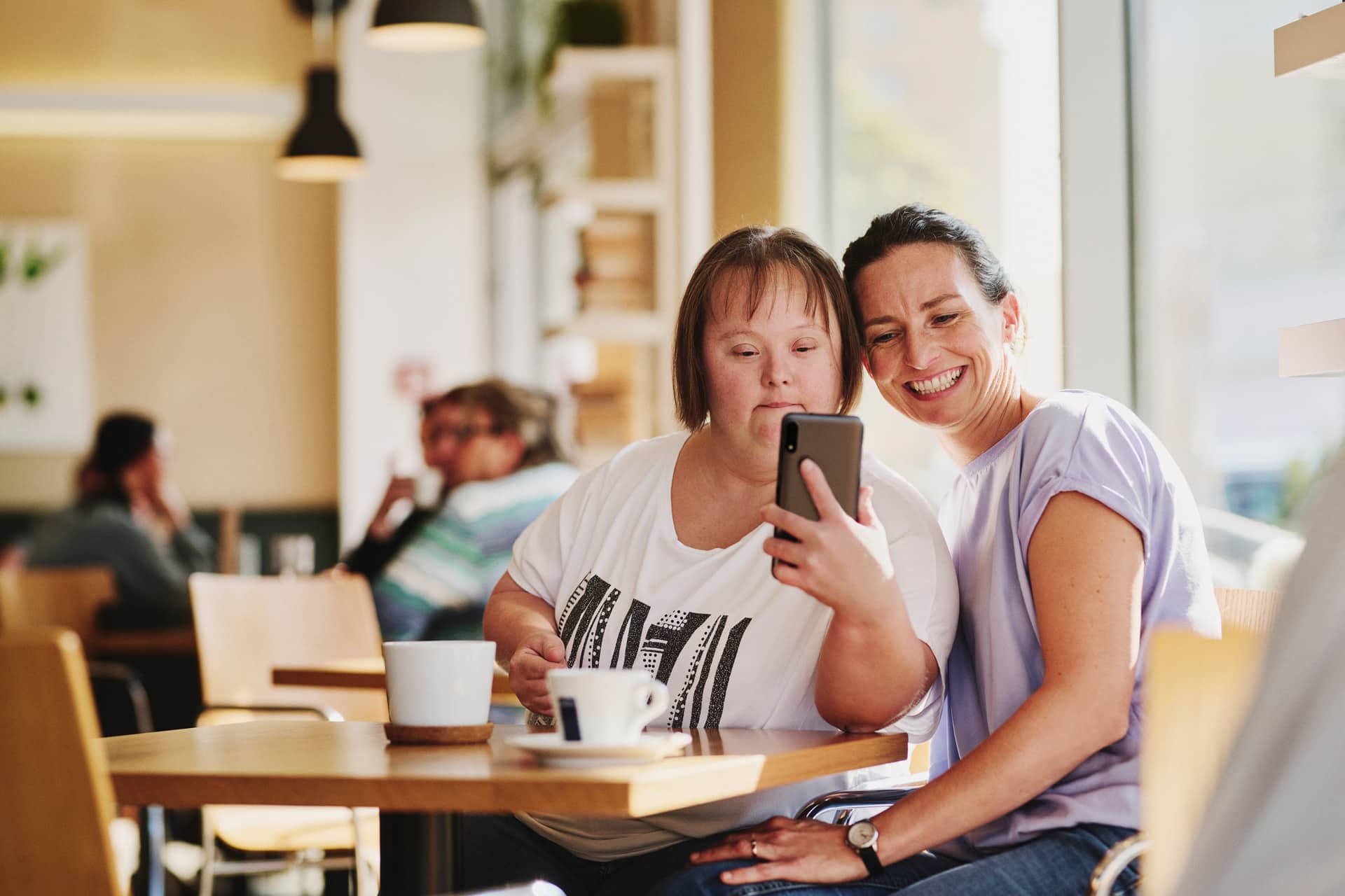 Frau mit Downsyndrom mit Freizeitassistentin in Café, machen Selfie von sich