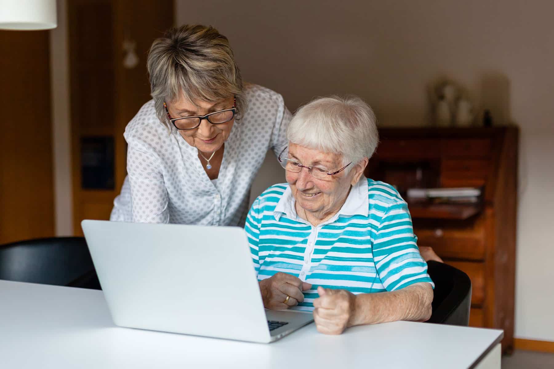 LebensGroß Begleiterin zeigt älterer Frau den Umgang mit einem Laptop