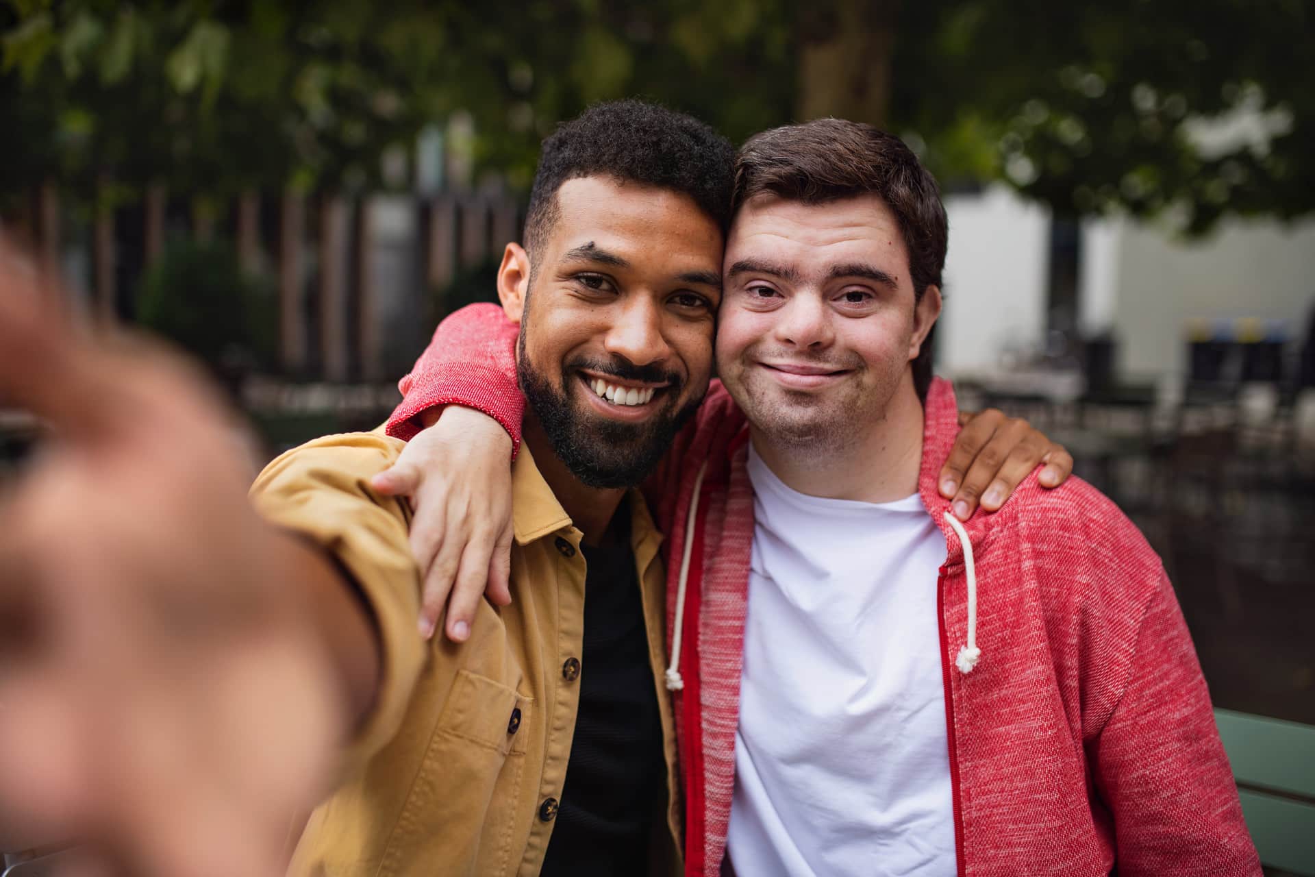 zwei junge Männer, einer mit Downsyndrom machen lachend Selfie von sich