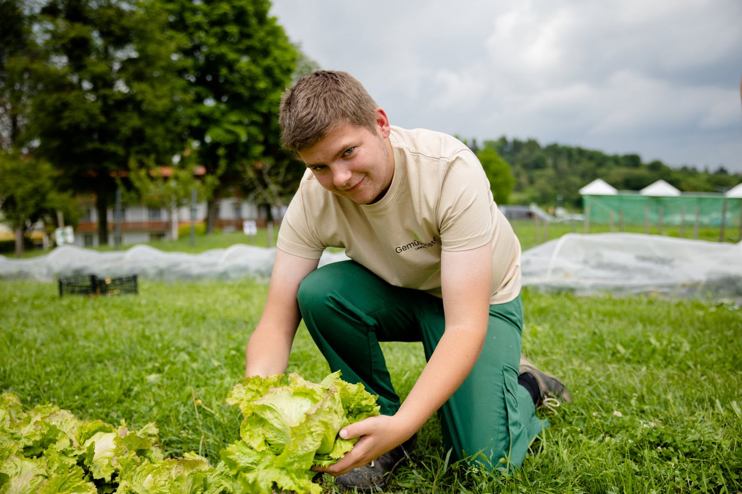 junger Gärtner kniet mit Salat in Händen am LebensGroß-Acker