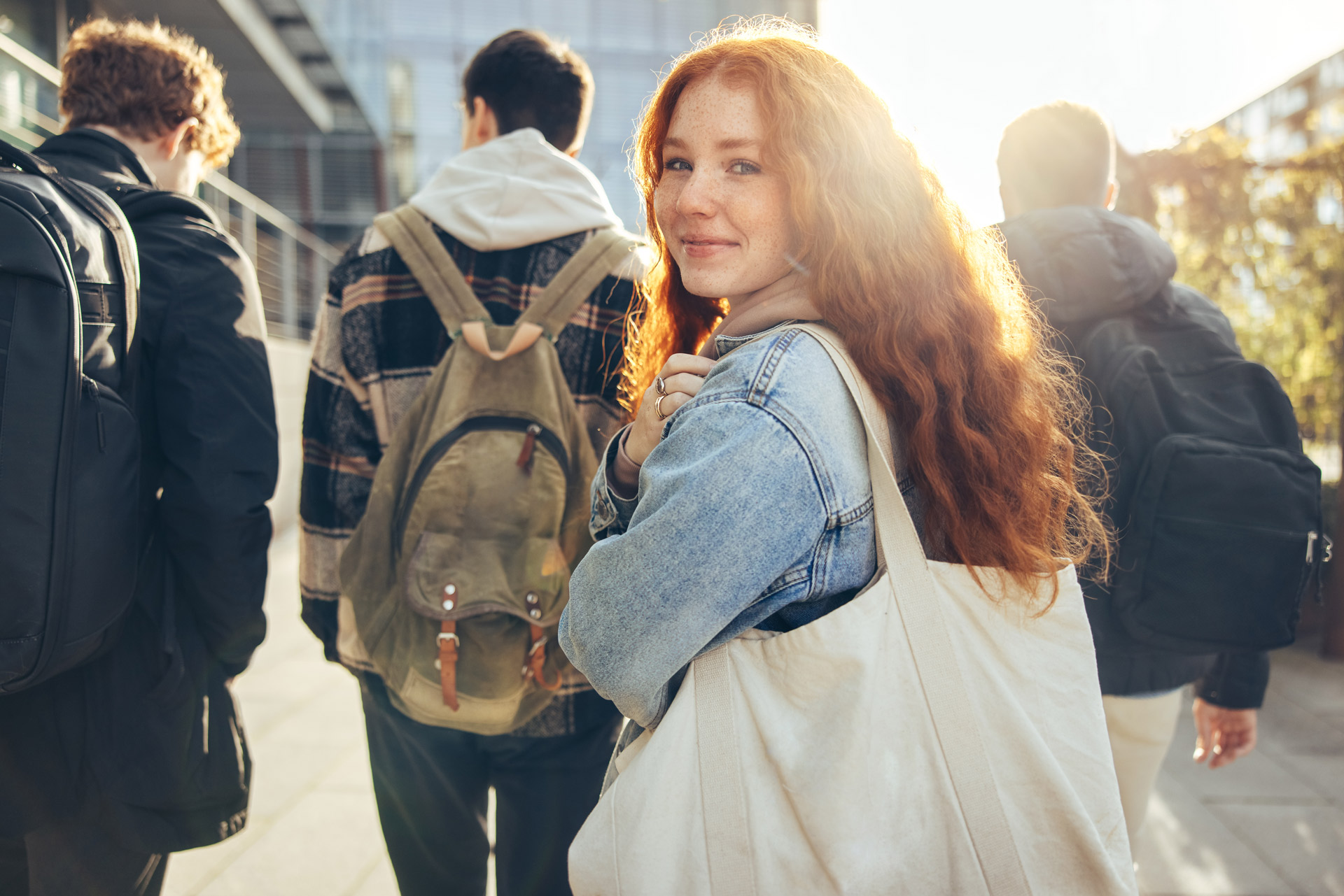 weiblicher Teenager mit Schultasche aus Stoff geht mit Freunden in die Schule
