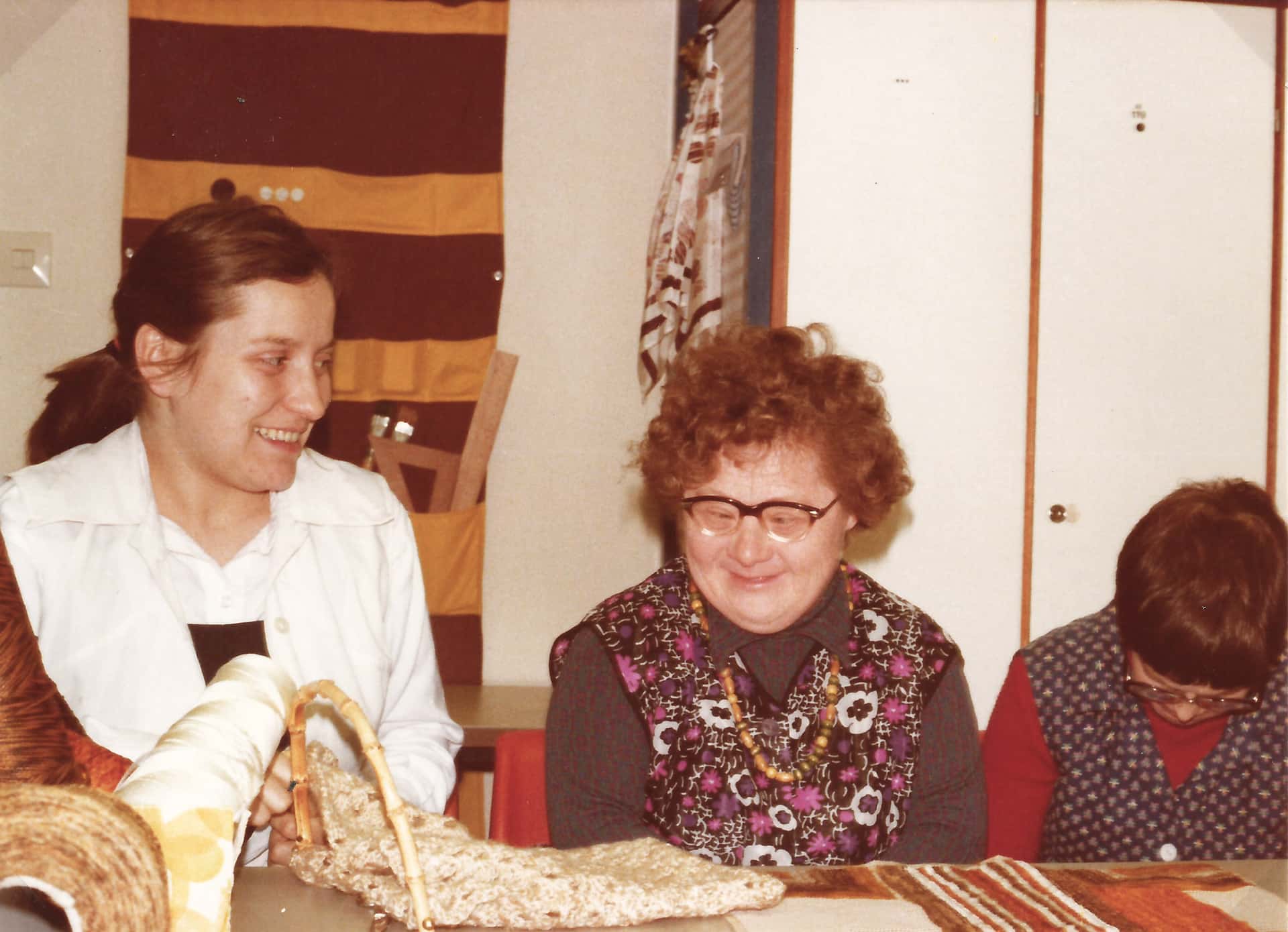 Drei Frauen sitzen an Tisch, eine davon mit Downsyndrom, altes Bild aus dem Jahr 1960