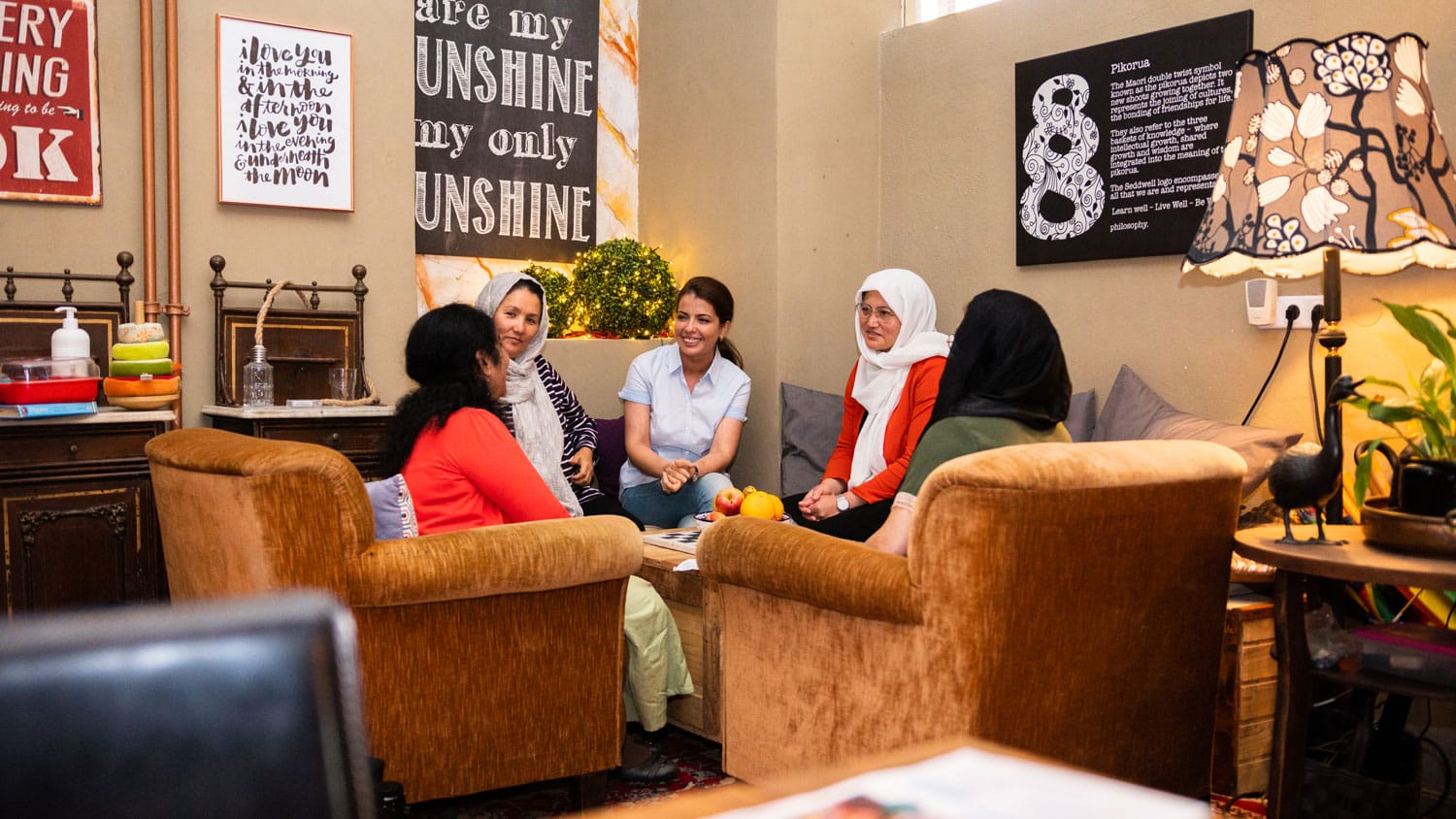 Vier Frauen, zwei davon tragen ein Kopftuch sitzen bei dem erfa-Nachbarschaftstreff gemütlich in Wohnzimmer beisammen