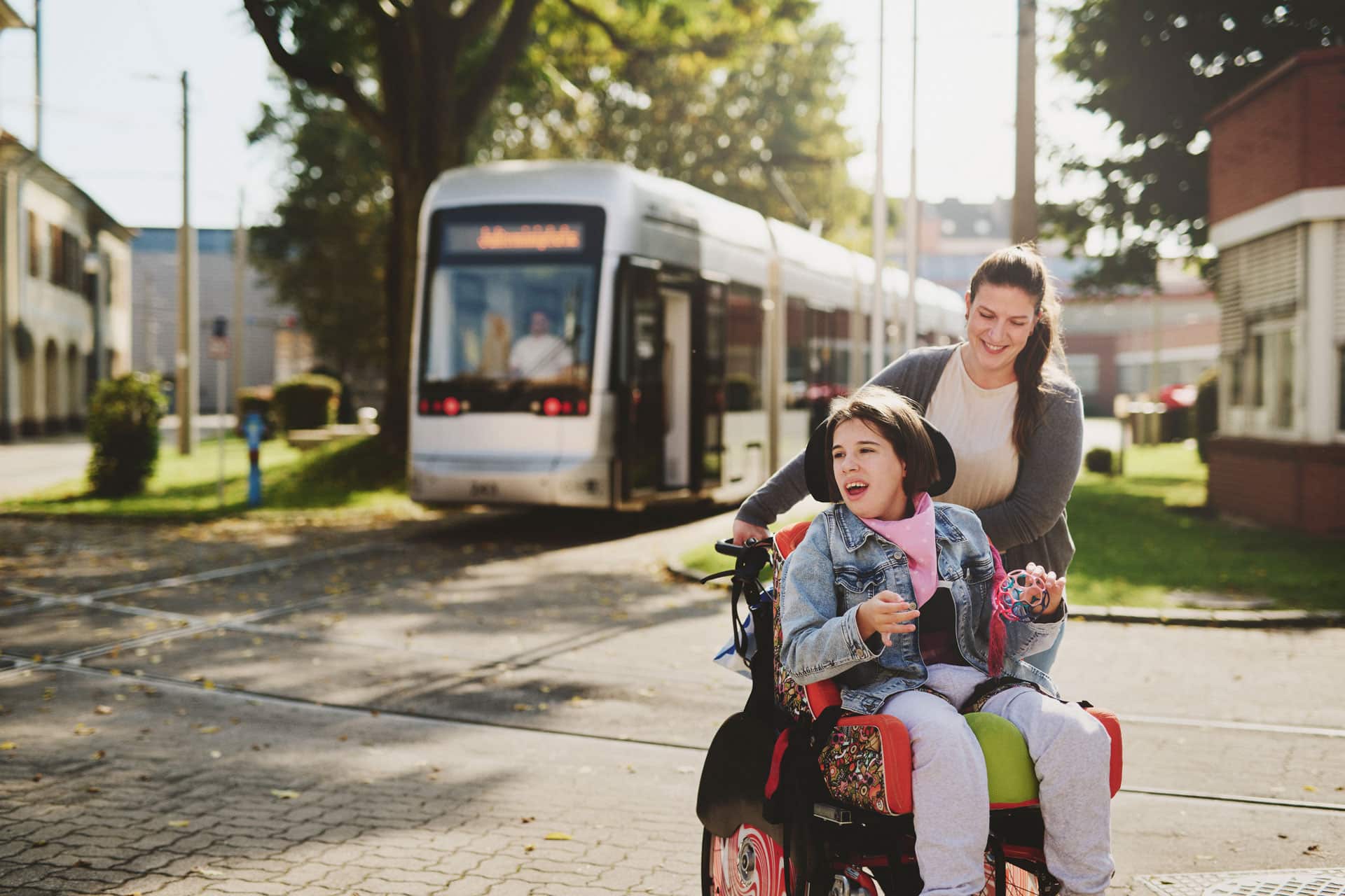 LebensGroß Begleiterin schiebt Mädchen im Rollstuhl aus öffentlichem Verkehrsmittel