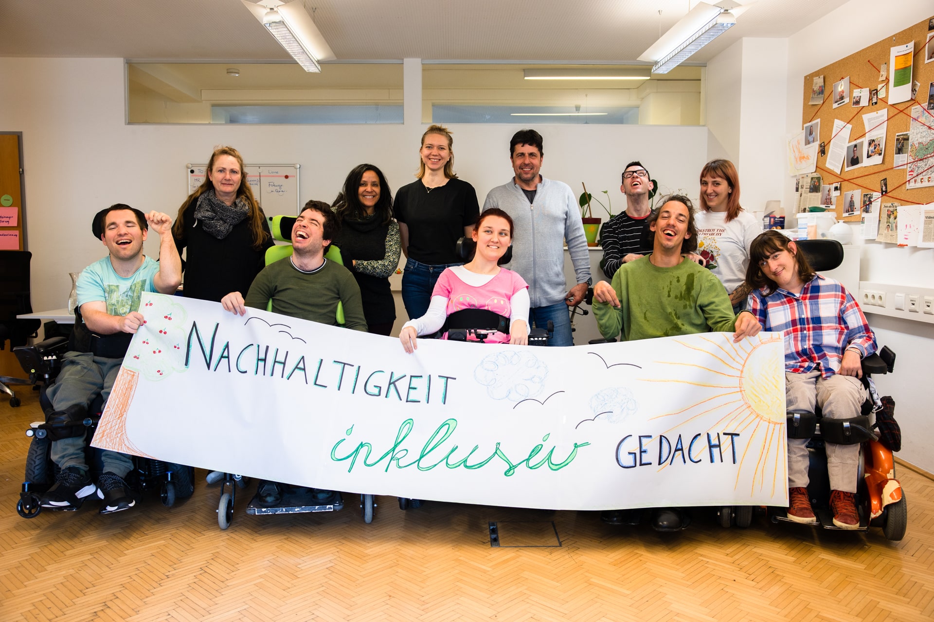 Menschengruppe stehend und sitzend in Rollstühlen mit Plakat in Händen mit Aufschrift "Nachhaltigkeit inklusiv gedacht"