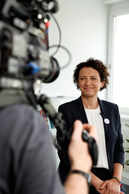LebensGroß Geschäftsführerin Susanne Maurer-Aldrian stehend vor Filmkamera