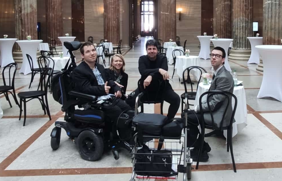 drei Männer, einer davon im Rollstuhl, einer mit Rollator und eine Frau sitzend im österreichischen Parlament
