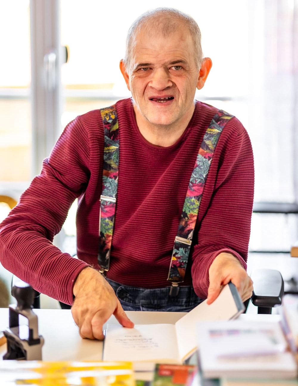 Mann mit Behinderungen sitzt an Tisch und arbeitet an einem Buch