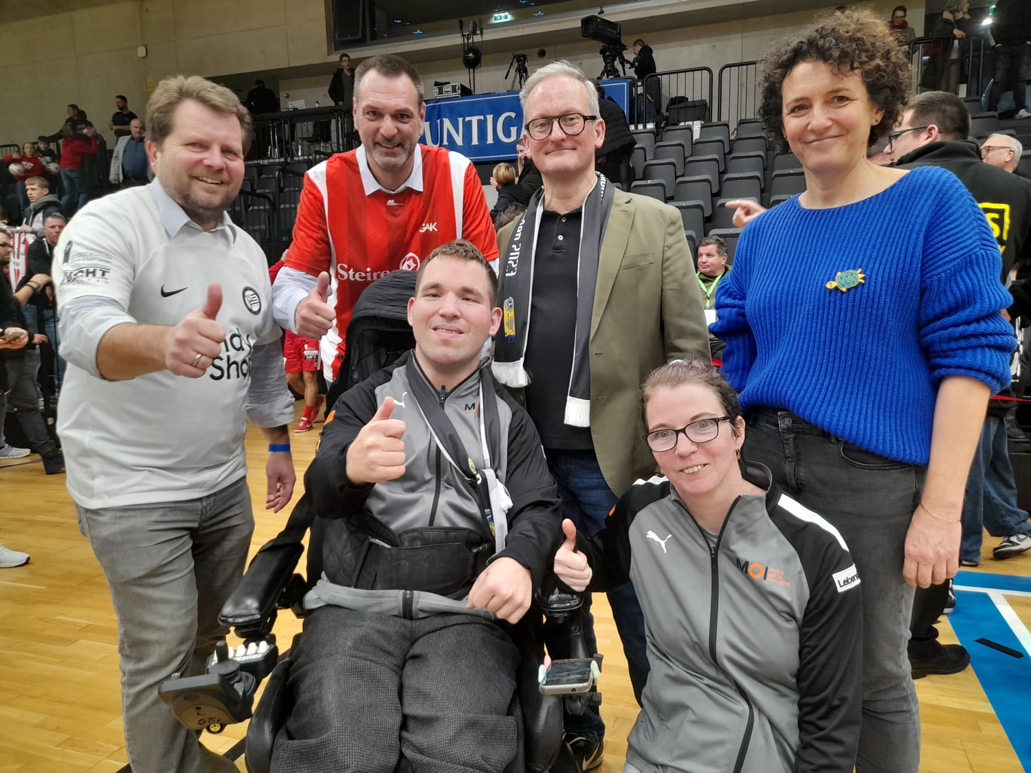 zwei Frauen und vier Männer, einer davon im Rollstuhl, machen in Fußballhalle ein gemeinsames Gruppenfoto