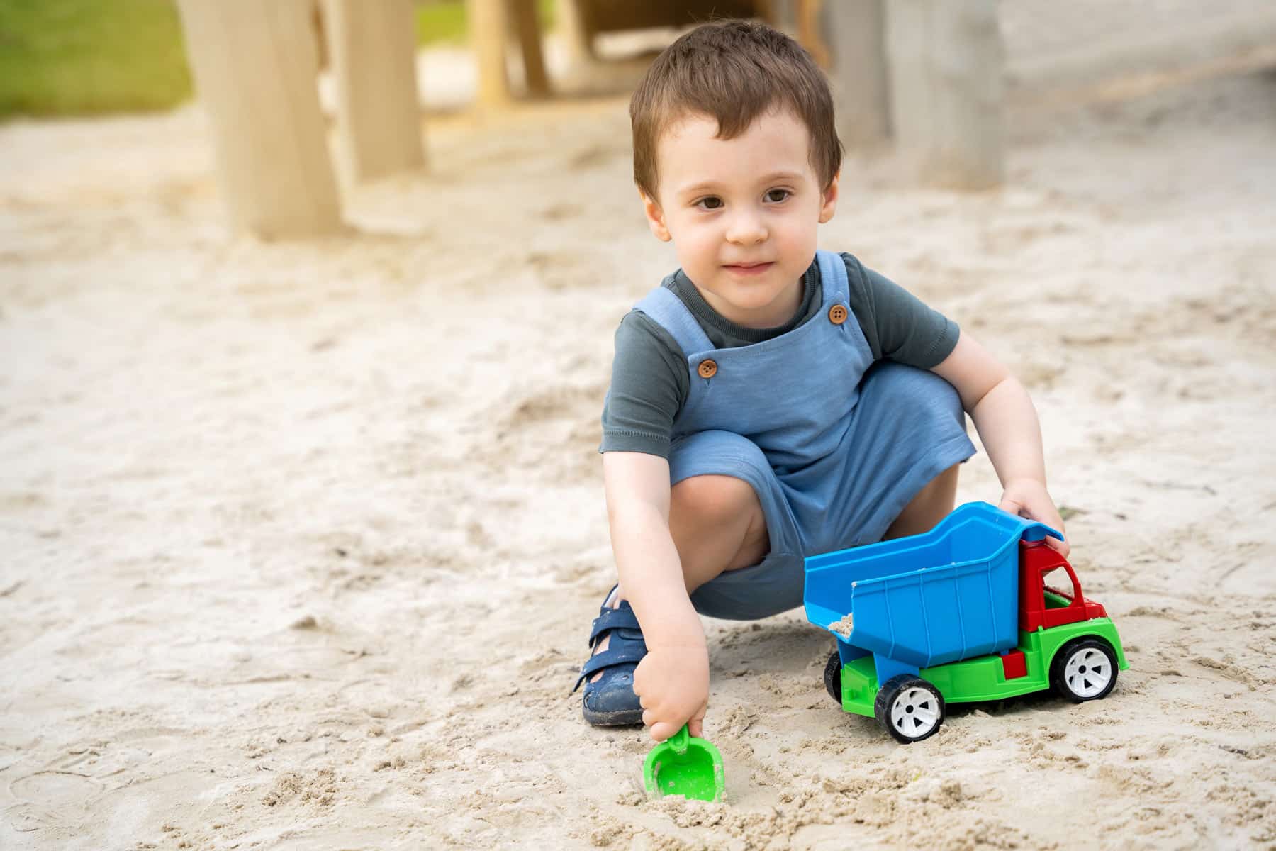 Ein Junge spielt mit einem Lastwagen in einer Sandkiste.